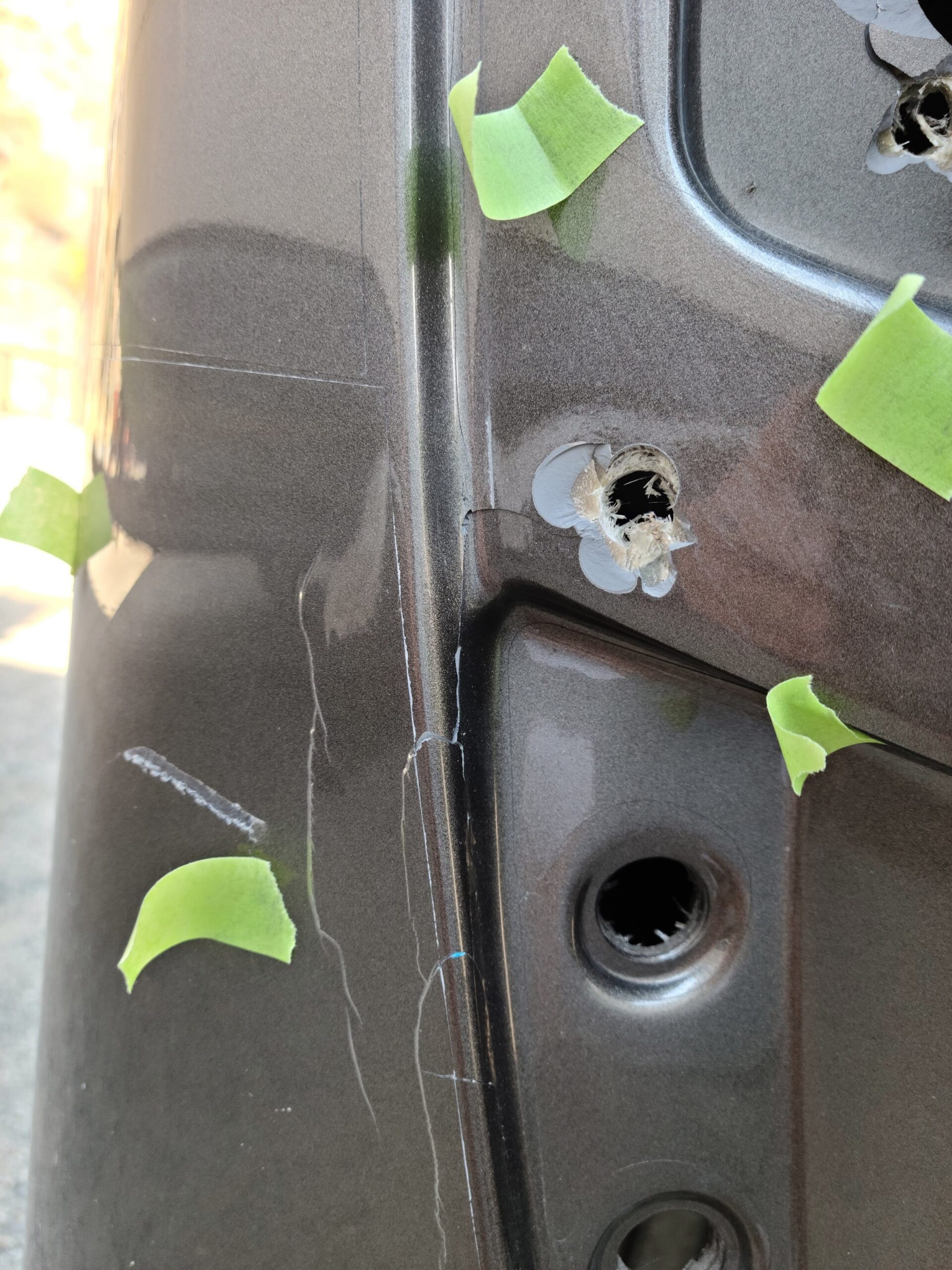 Close-up of holes in a dark motorhome front corner, marked with green tape before repair