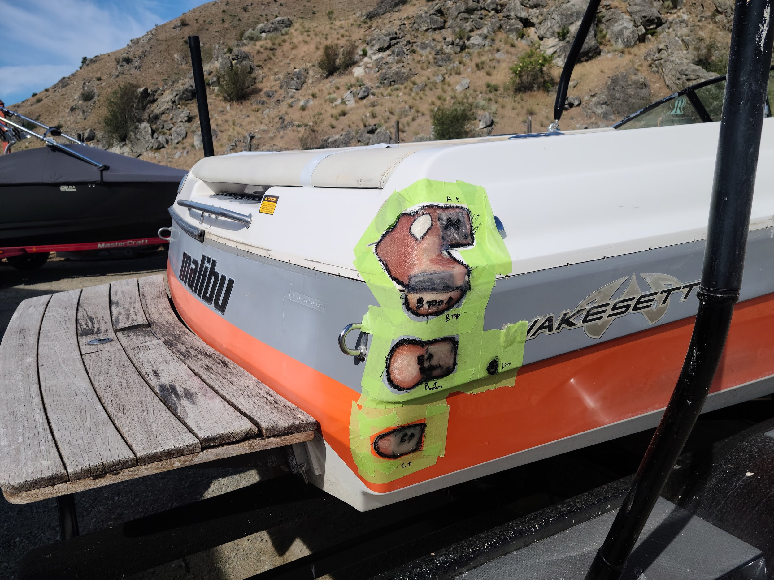 Wakeboat stern with three taped-off gelcoat divots across the gray panel and orange stripe